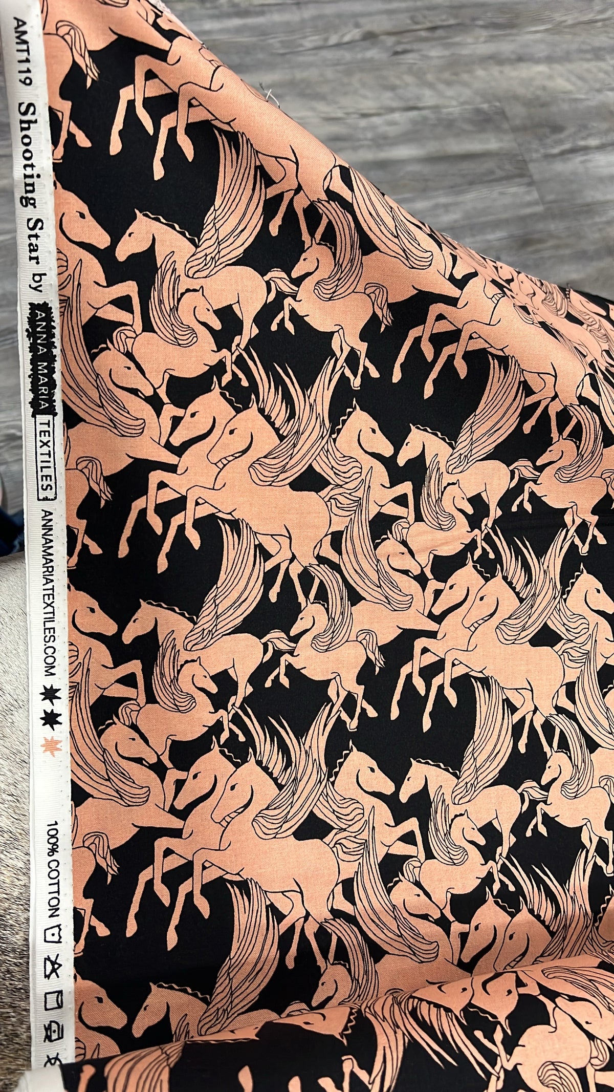 Shooting Star Mythology Pegasus fabric by Anna Maria, folded to show the horse print texture in peach on black